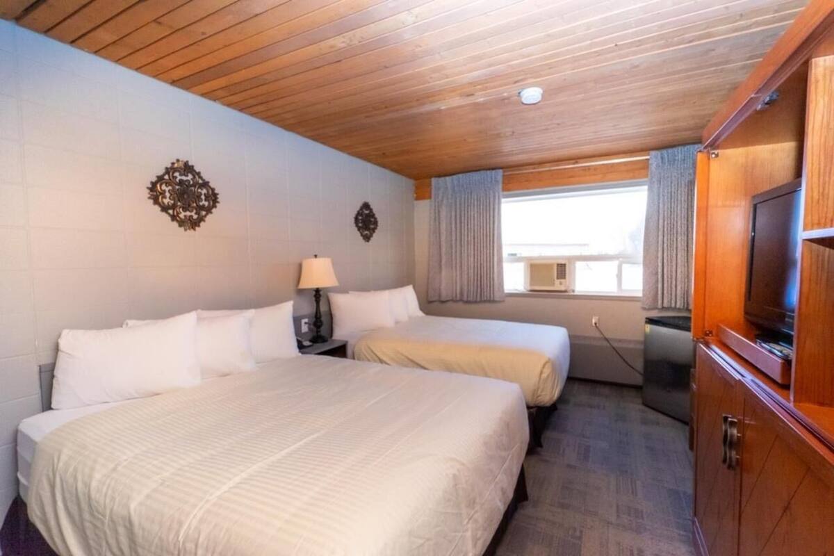Une chambre d’hôtel avec deux lits, un plafond en bois, une télévision et une fenêtre avec des rideaux.