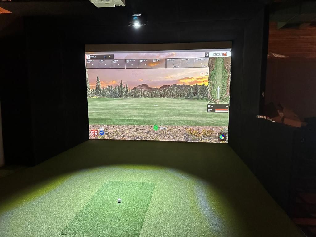 Configuración de simulación de golf con pantalla mostrando un campo de golf, un tapete verde y una pantalla montada en la pared.
