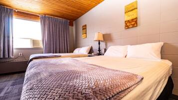 Habitación de hotel con techo de madera, dos camas con ropa blanca, una ventana con cortinas y una pared decorada con una obra enmarcada.