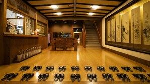 A hotel lobby with a wooden floor, a reception desk, a staircase, and a wall with artwork. - Mikuniya (Toyooka)