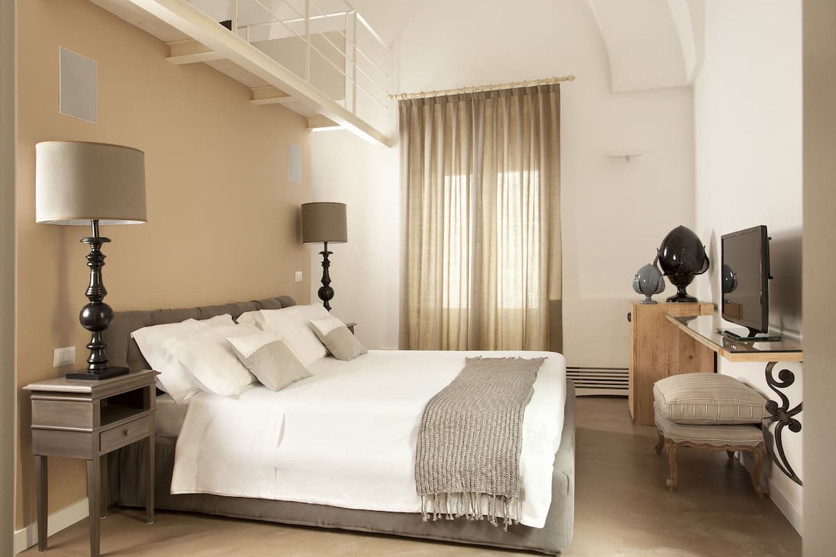 A bedroom with a large bed, two bedside tables with lamps, a TV, and a small wooden cabinet.