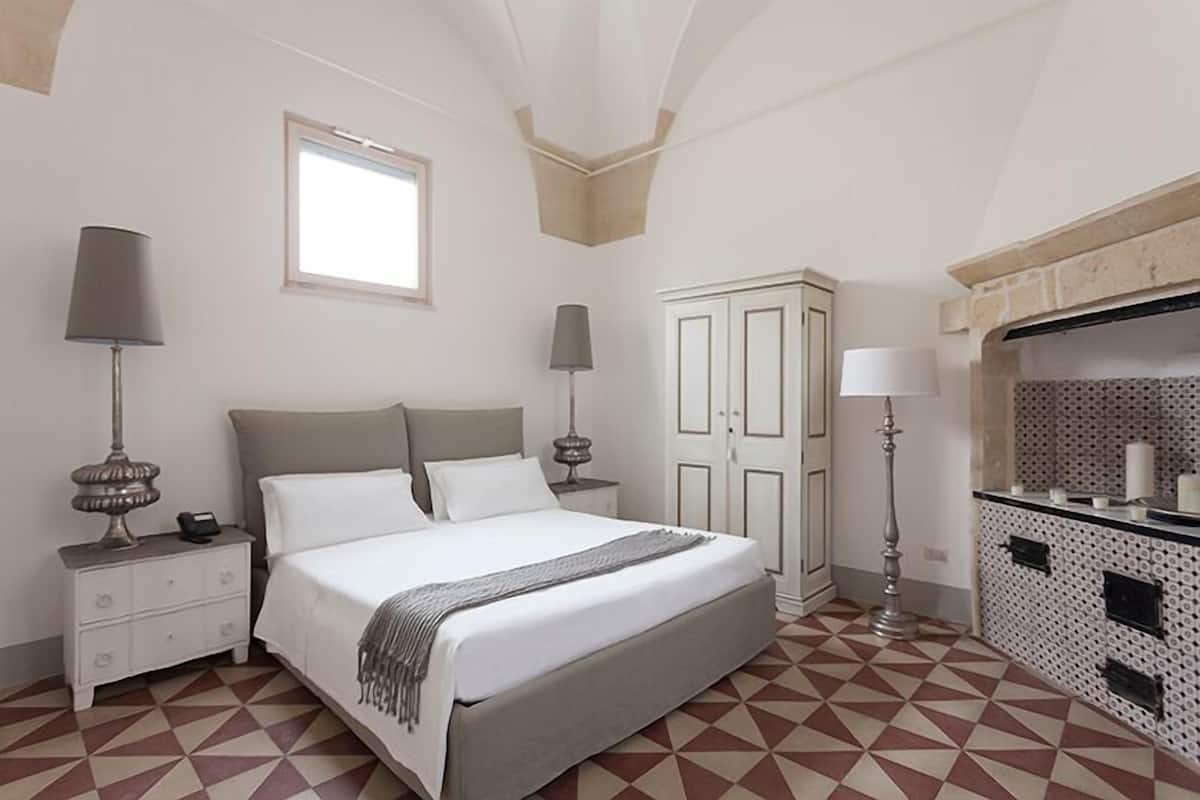 A bedroom with a bed, nightstands, a dresser, and a bathroom with a tiled backsplash.