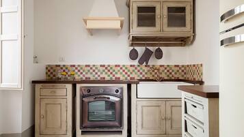 A kitchen with a tiled backsplash, a stove, cabinets, and a hanging pot rack.