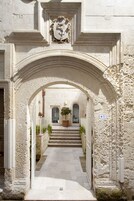 Una entrada arqueada a un edificio con fachada de piedra, un escudo heráldico sobre el arco y una escalera que lleva a una puerta.