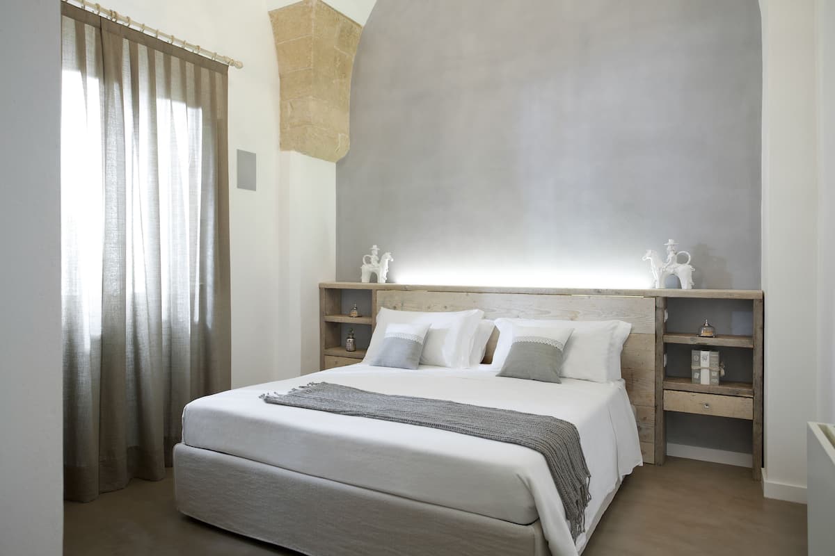 A bedroom with a large bed, wooden headboard, bedside tables, and a window with curtains.