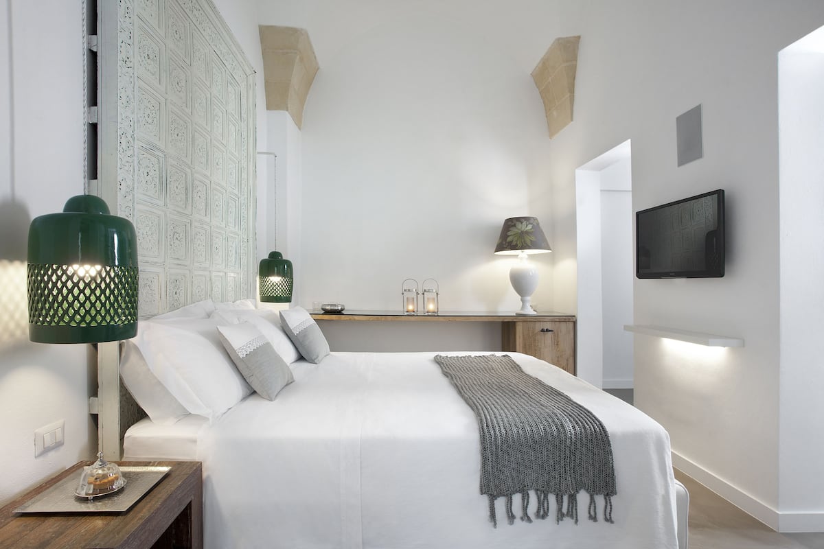 A modern bedroom with a large bed, two bedside tables, a nightstand, a wall-mounted TV, and a decorative wall panel.