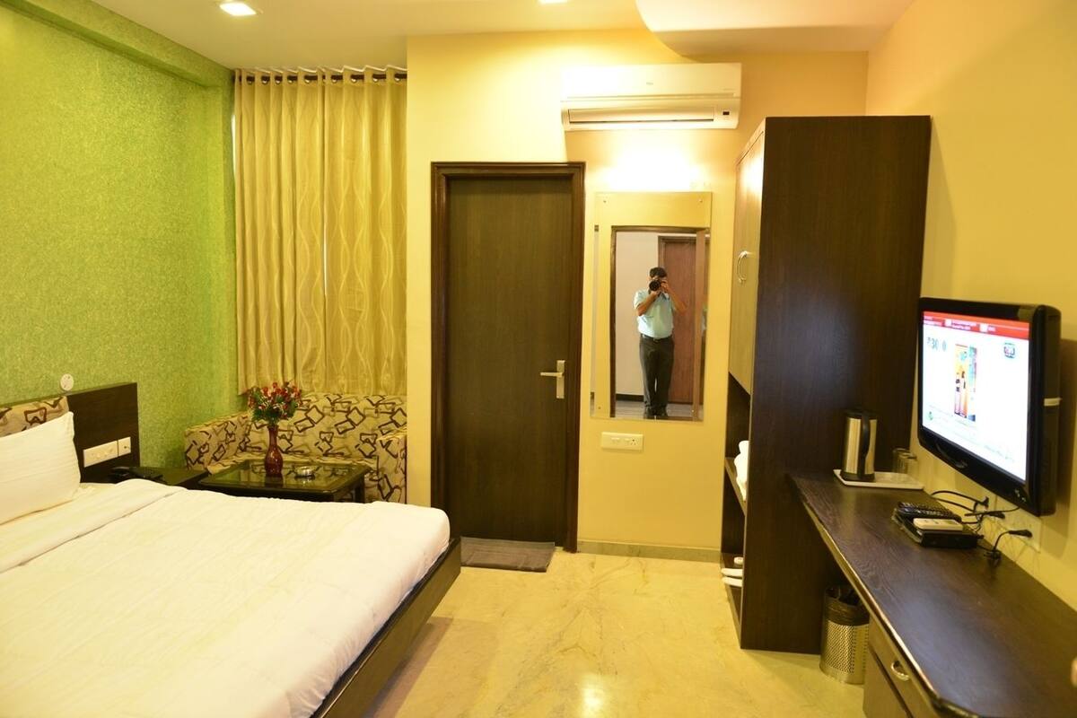 A hotel room with a bed, a desk with a television, a mirror, and a door leading to another room.