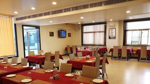 A conference room with multiple tables set for dining, equipped with chairs, plates, cutlery, and placemats. - Royal View Hotel (Jaipur)