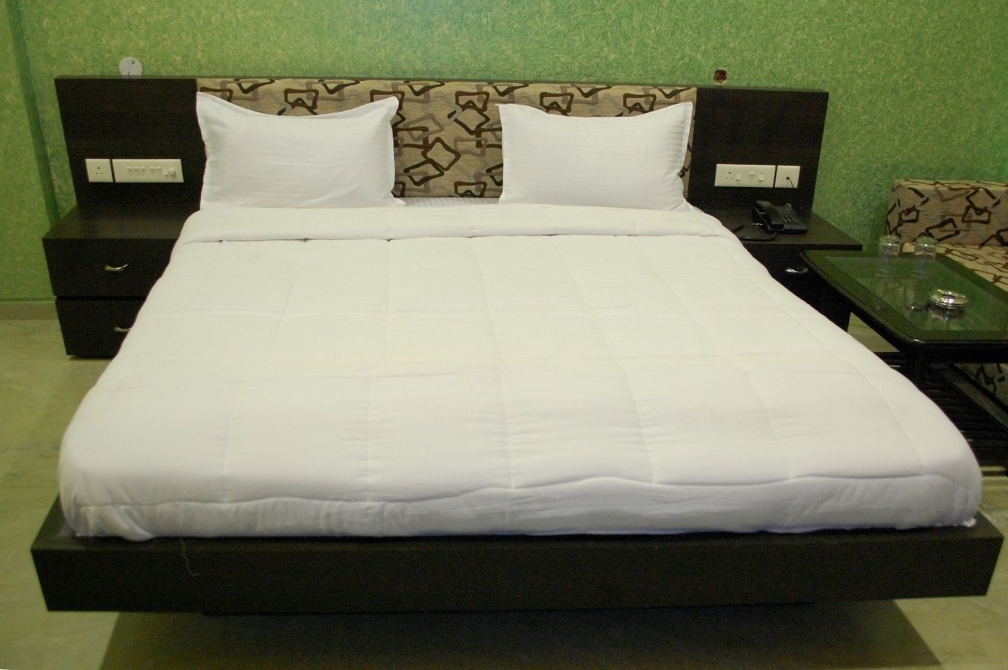 A large bed with white bedding, two bedside tables, and a patterned headboard.