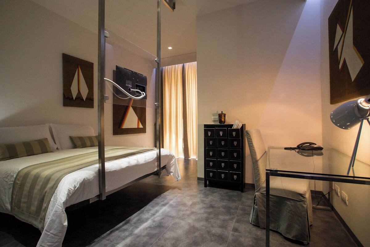 Une chambre d’hôtel moderne avec un grand lit, un bureau avec une chaise, une armoire et une lampe de bureau.