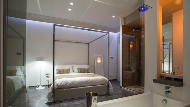 A modern bedroom with a large bed, a glass-enclosed shower, and a separate bathroom with a bathtub. - Hotel Santa Brigida (Naples)
