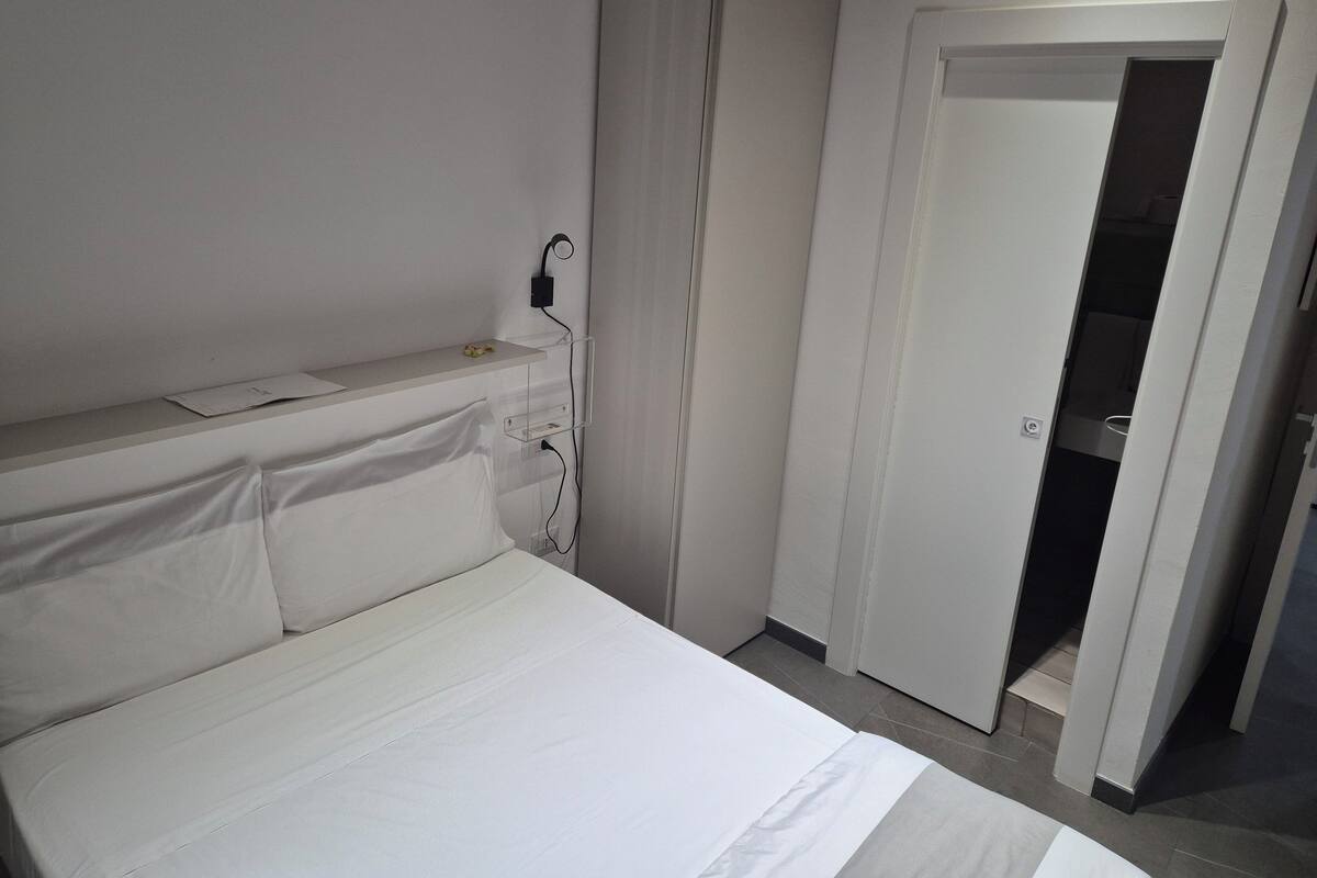 Une chambre d’hôtel comprenant un lit, une table de chevet, une prise de courant fixée au mur et une porte donnant sur un placard.