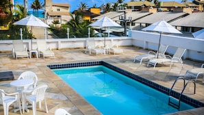 Zona de piscina al terrat amb gandules i ombrelles, envoltada d'un paviment de rajoles i amb vista a una zona residencial.