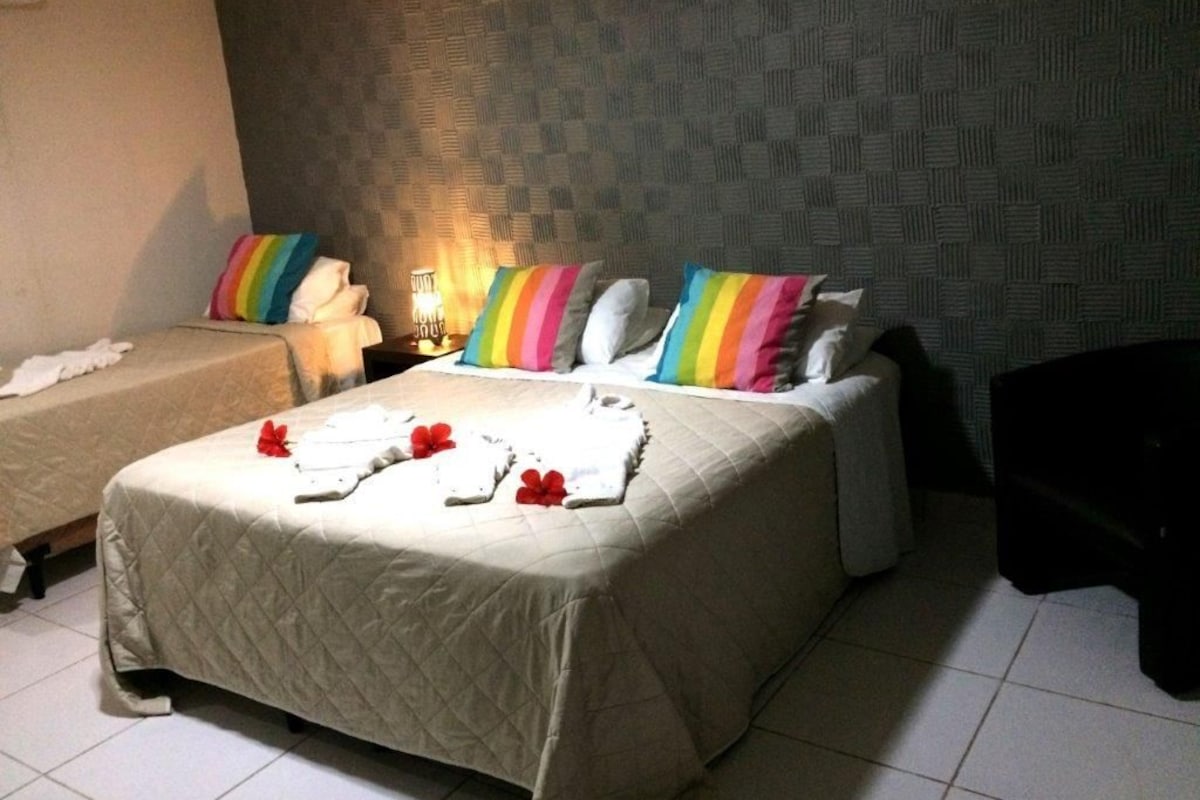 Habitación de hotel con dos camas, una mesita de noche, una lámpara y un sillón oscuro.