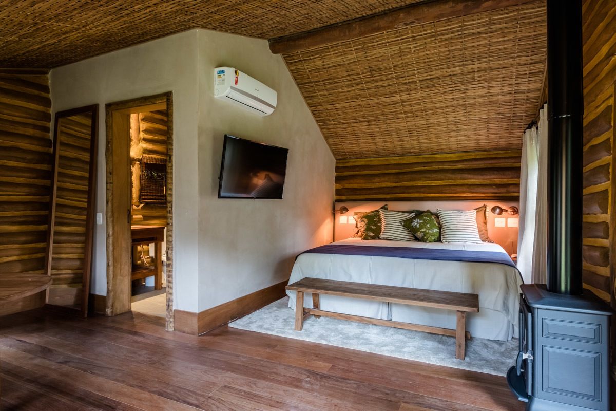 Un dormitorio acogedor con techo de madera, cama con banco, televisor y chimenea.