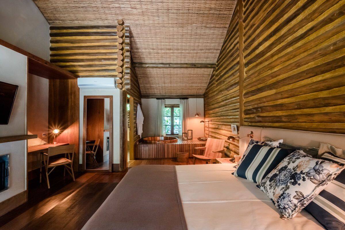Un dormitorio acogedor con techo de madera, una cama grande con almohadones florales, un escritorio con una silla y vistas a un baño con lavamanos circular.