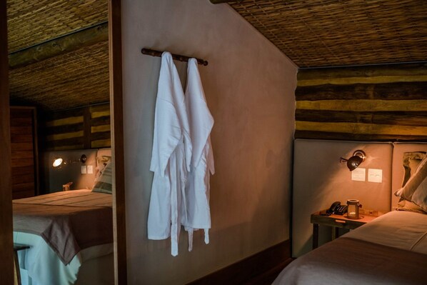 A cozy room with a wooden ceiling, a bed with white linens, a bedside table with a lamp, and a wall-mounted towel rack.