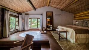 A room with a wooden ceiling, a large window, a bed, a small table, and a wooden chair. - Pousada Tankamana (Petrópolis)