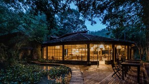 A traditional Japanese-style building with a wooden deck, surrounded by lush greenery and a pond. - Pousada Tankamana (Petrópolis)