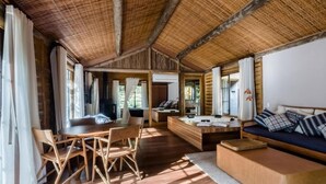 A spacious room with a wooden ceiling, a dining area with chairs and a table, a sofa with cushions, and a large window providing natural light. - Pousada Tankamana (Petrópolis)