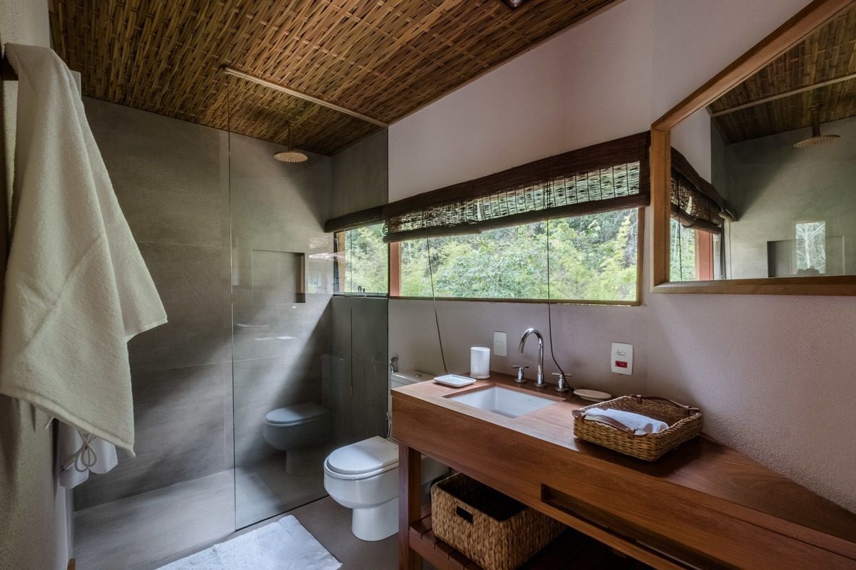 Un baño moderno con cabina de ducha de vidrio, tocador de madera, un espejo grande y vistas al exterior a través de una ventana.