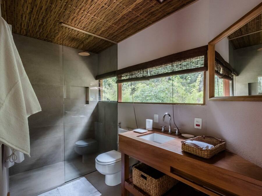 Un baño moderno con cabina de ducha de vidrio, tocador de madera, un espejo grande y vistas al exterior a través de una ventana.