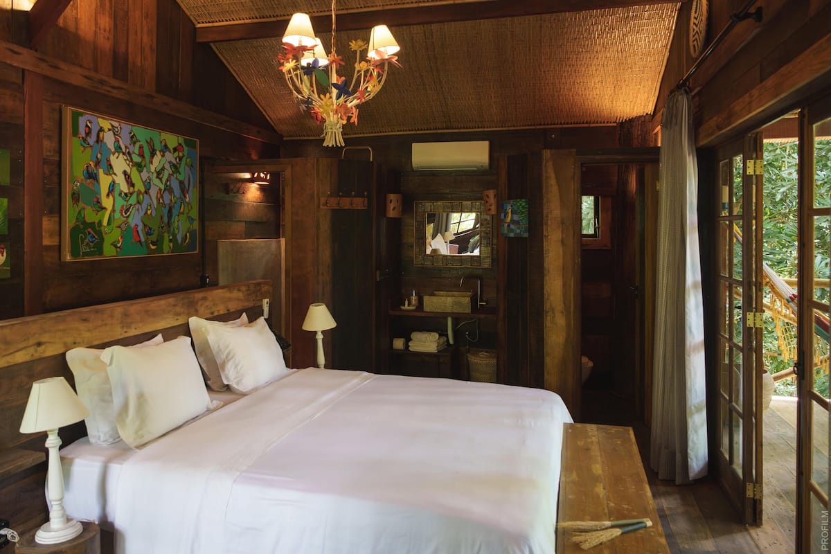 Una habitación de madera con una cama grande, una araña y obras de arte en las paredes.