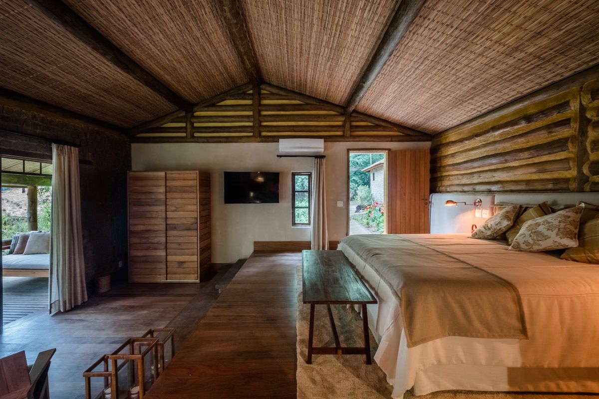 A bedroom with a wooden ceiling, a bed with pillows, a bench, and a TV.