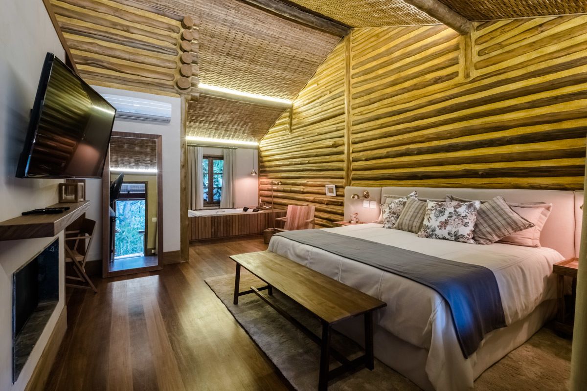 Un dormitorio acogedor con una cama grande, un banco, un televisor y un techo de madera.
