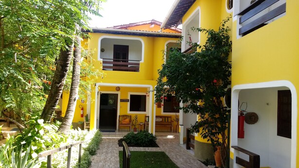 A yellow building with a paved courtyard, a reception area, and a staircase leading to an upper floor. - Aguamarinha Pousada (Ipojuca)