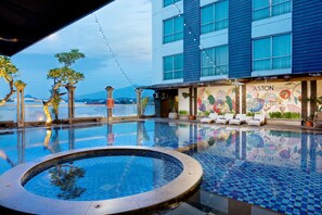 A hotel pool area with a view of a mountain, lounge chairs, and a mural on the building. - Aston Jember Hotel and Conference Center (Jember)