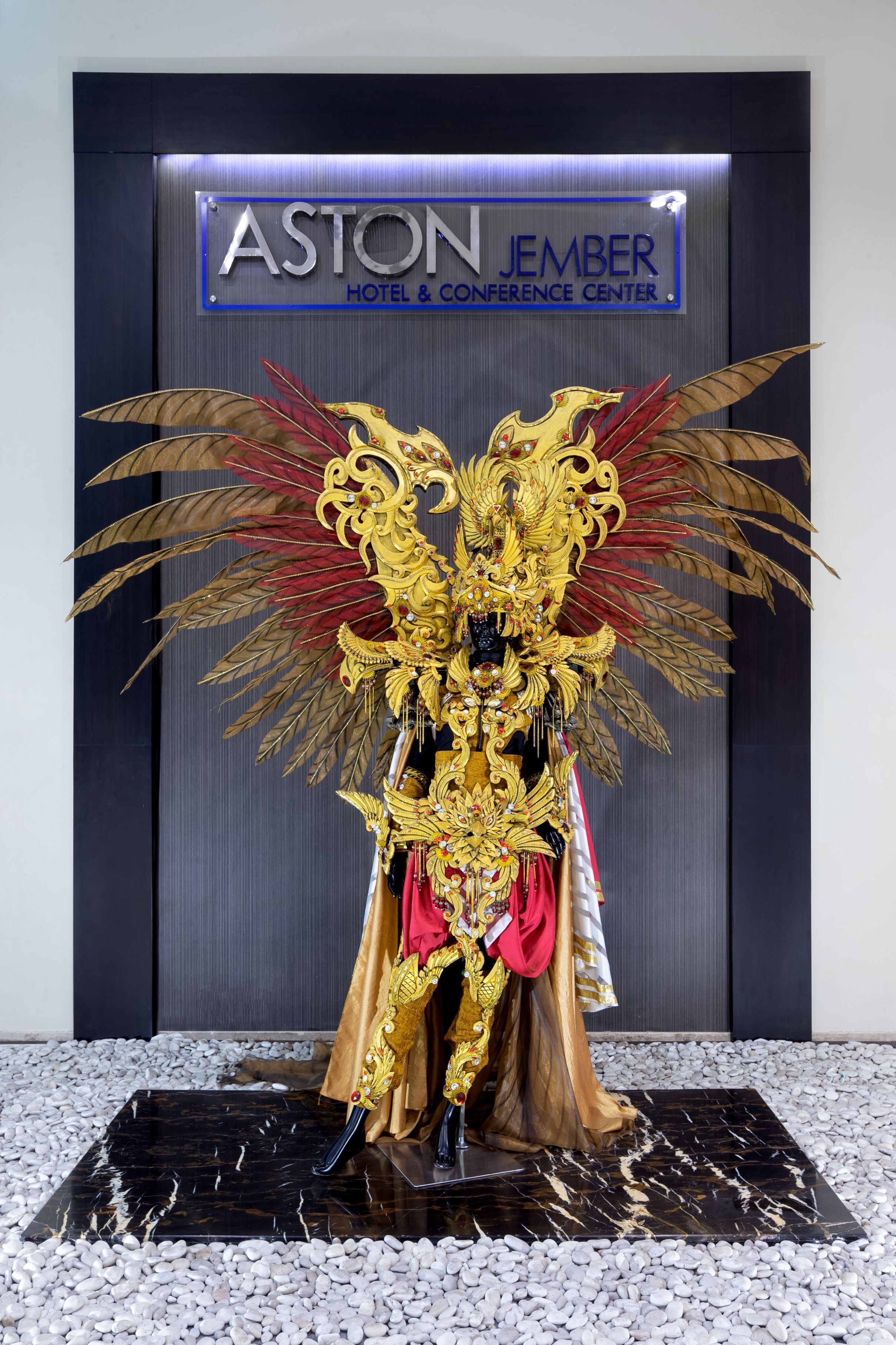 Una estatua dorada con elaboradas alas frente al letrero del Hotel & Centro de Convenciones Aston Jember.