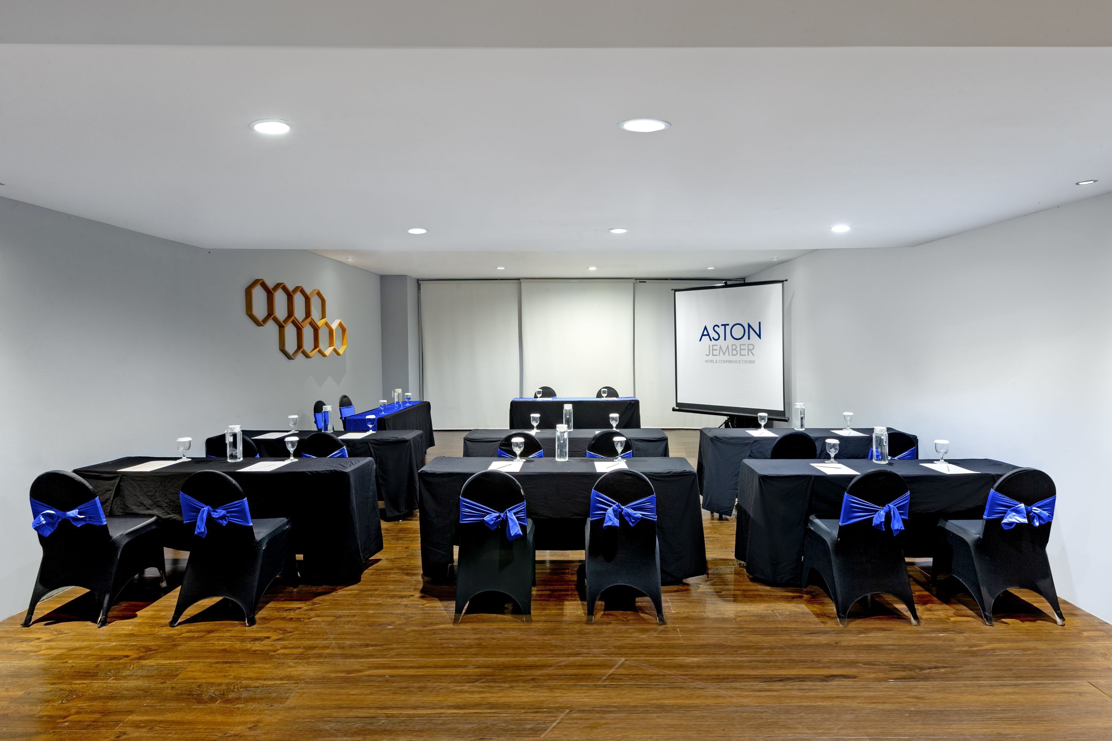 Une salle de conférence équipée de tables et de chaises, d’un écran de projection et d’un logo sur le mur.