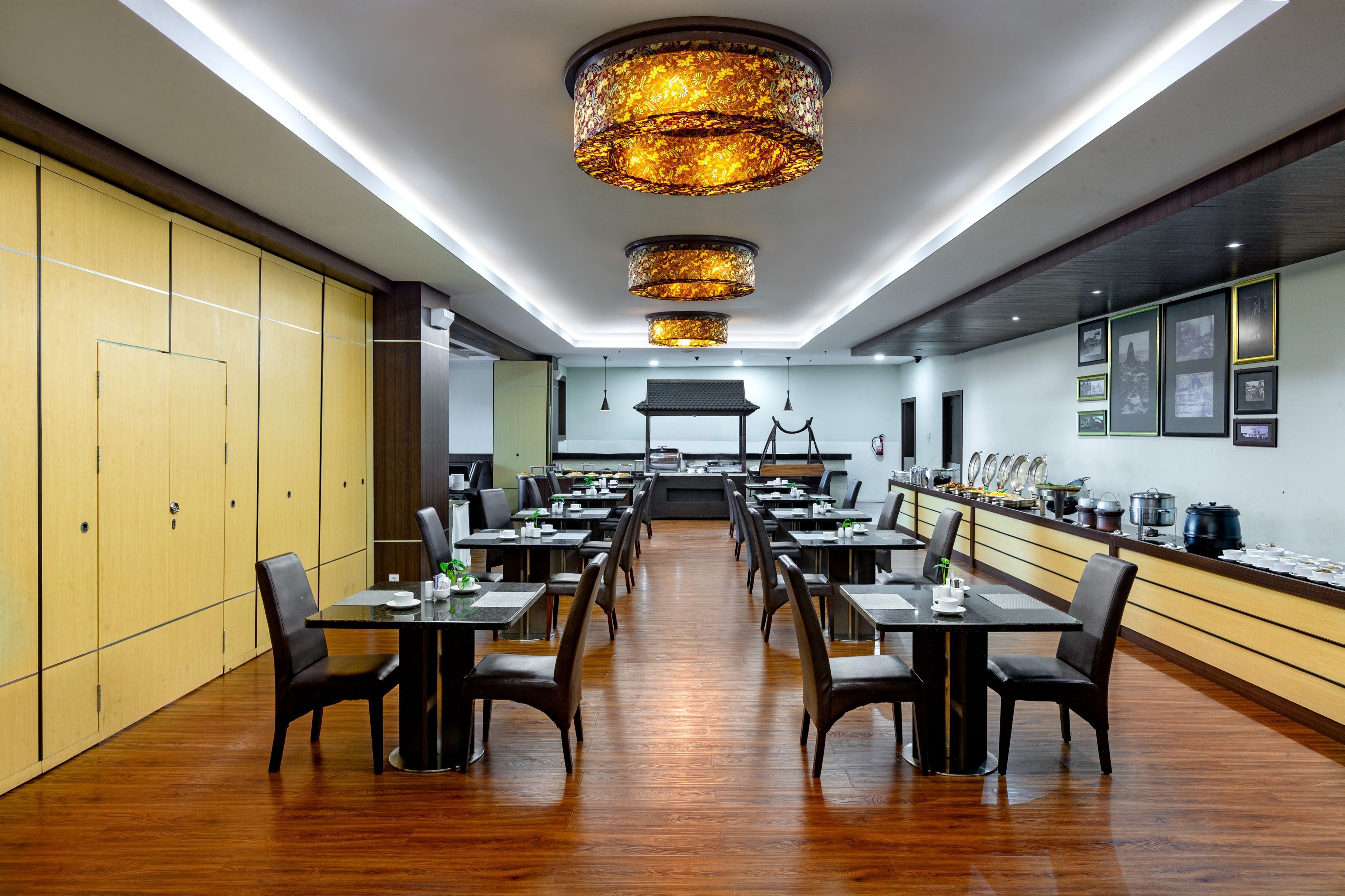 A spacious dining area with multiple tables and chairs, a long counter with kitchen equipment, and a traditional-style ceiling light fixture.