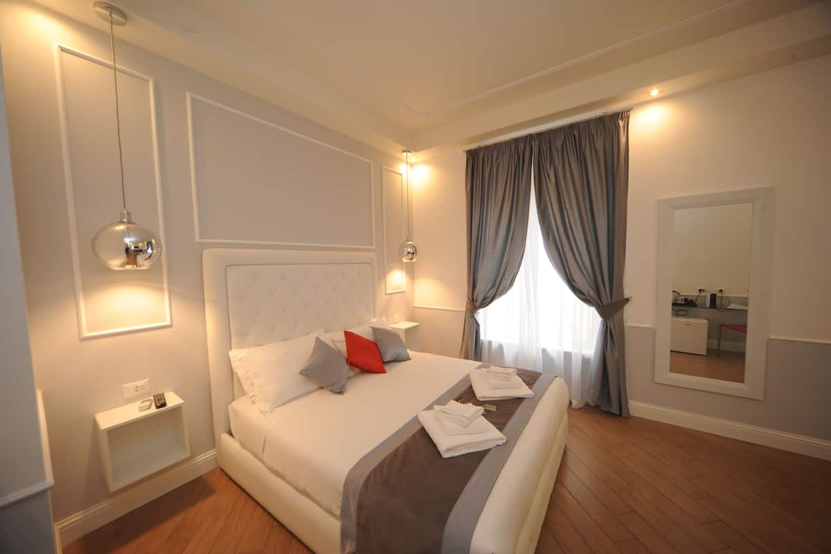 A hotel room with a neatly made bed, bedside tables, a mirror, and a window with curtains.