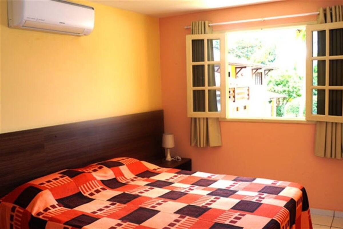 A room with a bed, a window with curtains, a bedside lamp, and an air conditioning unit.