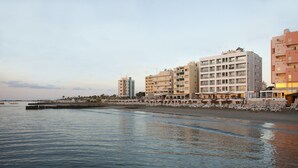 Een hotel aan het water met meerdere verdiepingen, een zwembadgedeelte en een promenade langs het strand.