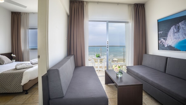 Een moderne hotelkamer met een bed, twee banken, een klein tafeltje en een balkon met uitzicht op zee.