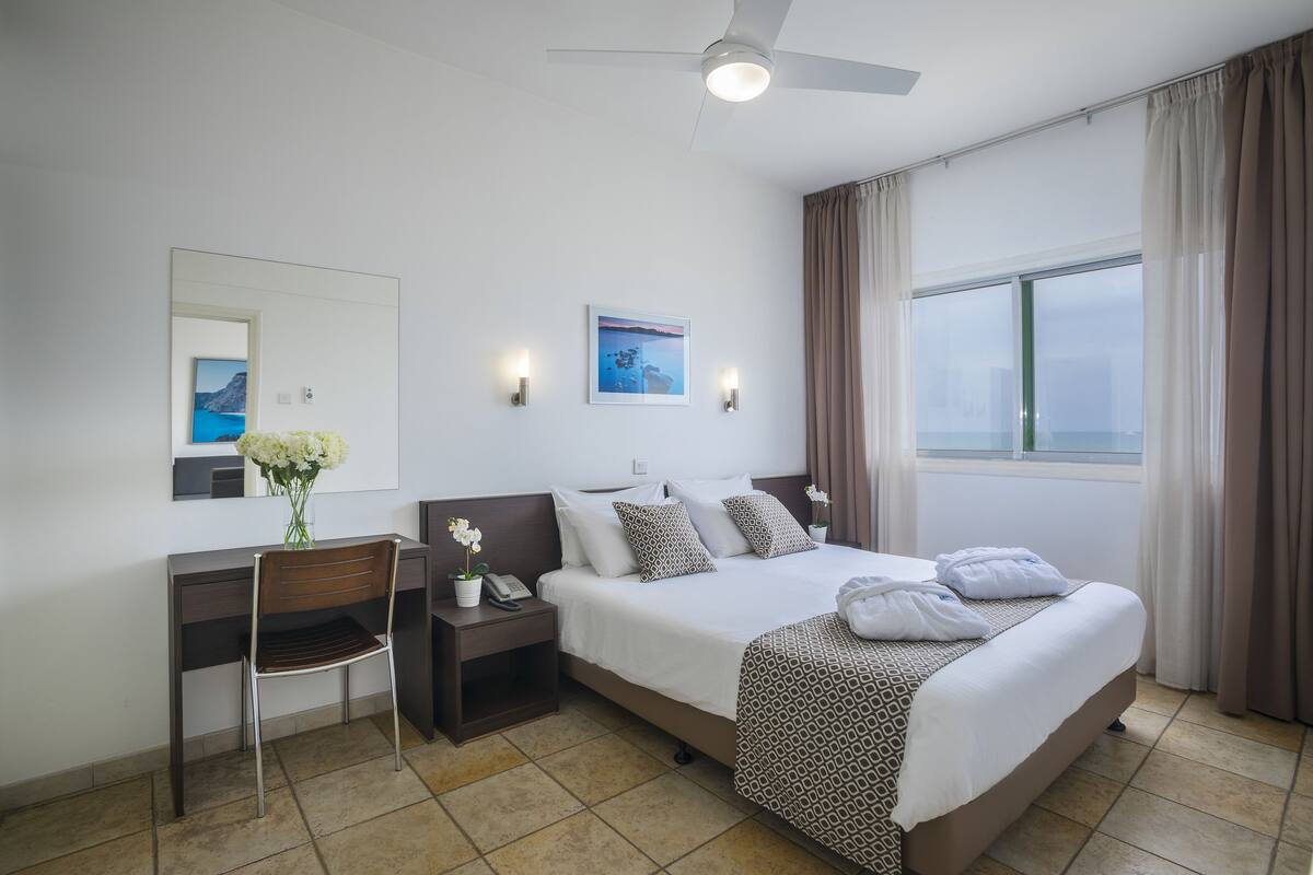 Ein Hotelzimmer mit Bett, Schreibtisch, Stuhl und einem Fenster mit Vorhängen.