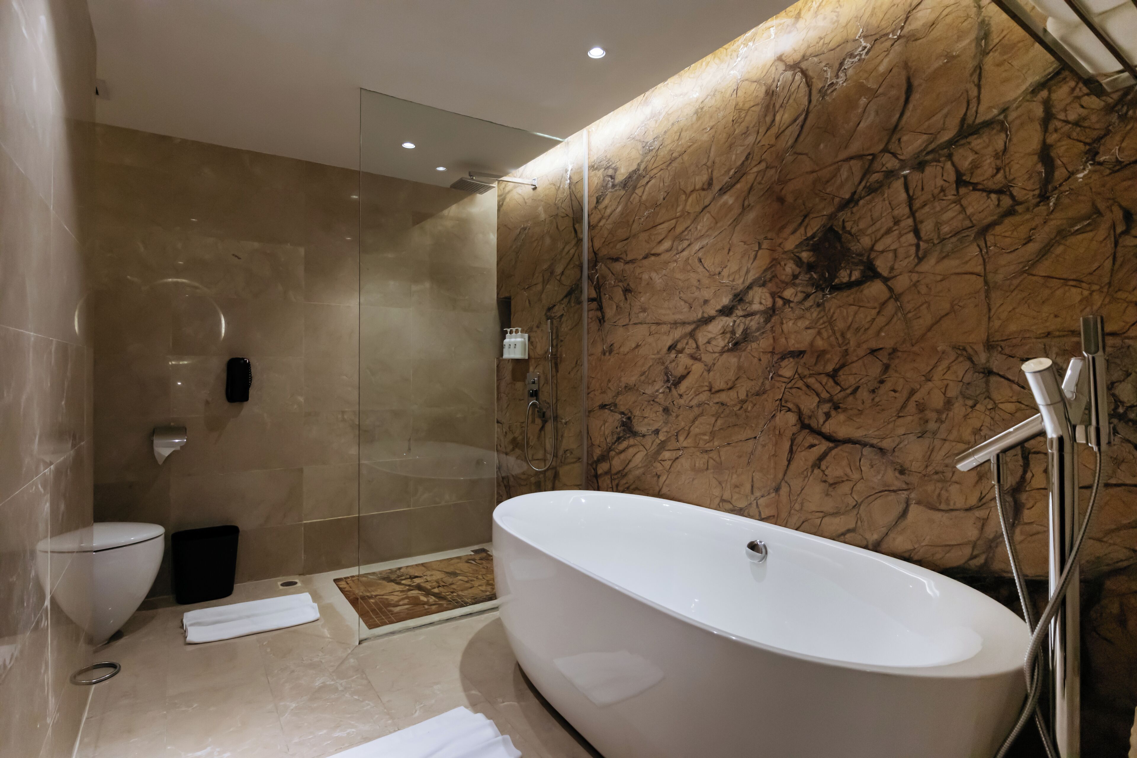 Un baño moderno con una bañera independiente, una ducha con cerramiento de vidrio y una pared de mármol.