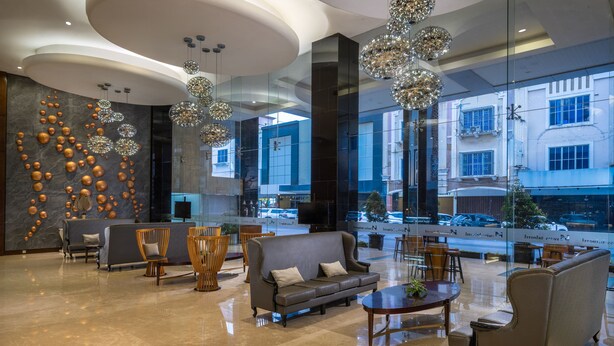 Een moderne lobby met een grijze bank, houten stoelen en een grote spiegel die het uitzicht naar buiten weerkaatst.
