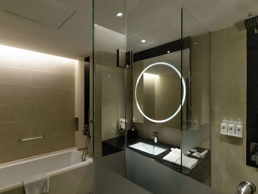 A modern bathroom with a glass-enclosed shower, a vanity with a sink, and a large mirror with a circular light.