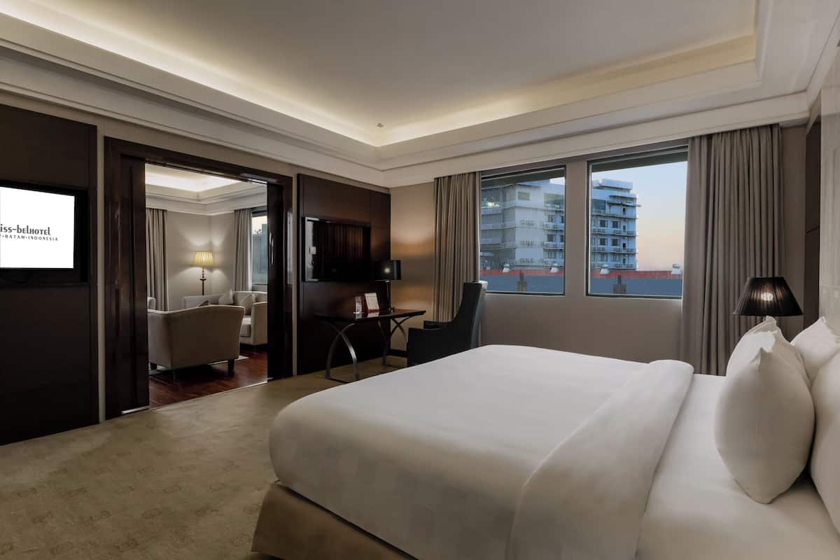 Een hotelkamer met een groot bed, een bureau met stoel, een televisie en uitzicht op de stad.