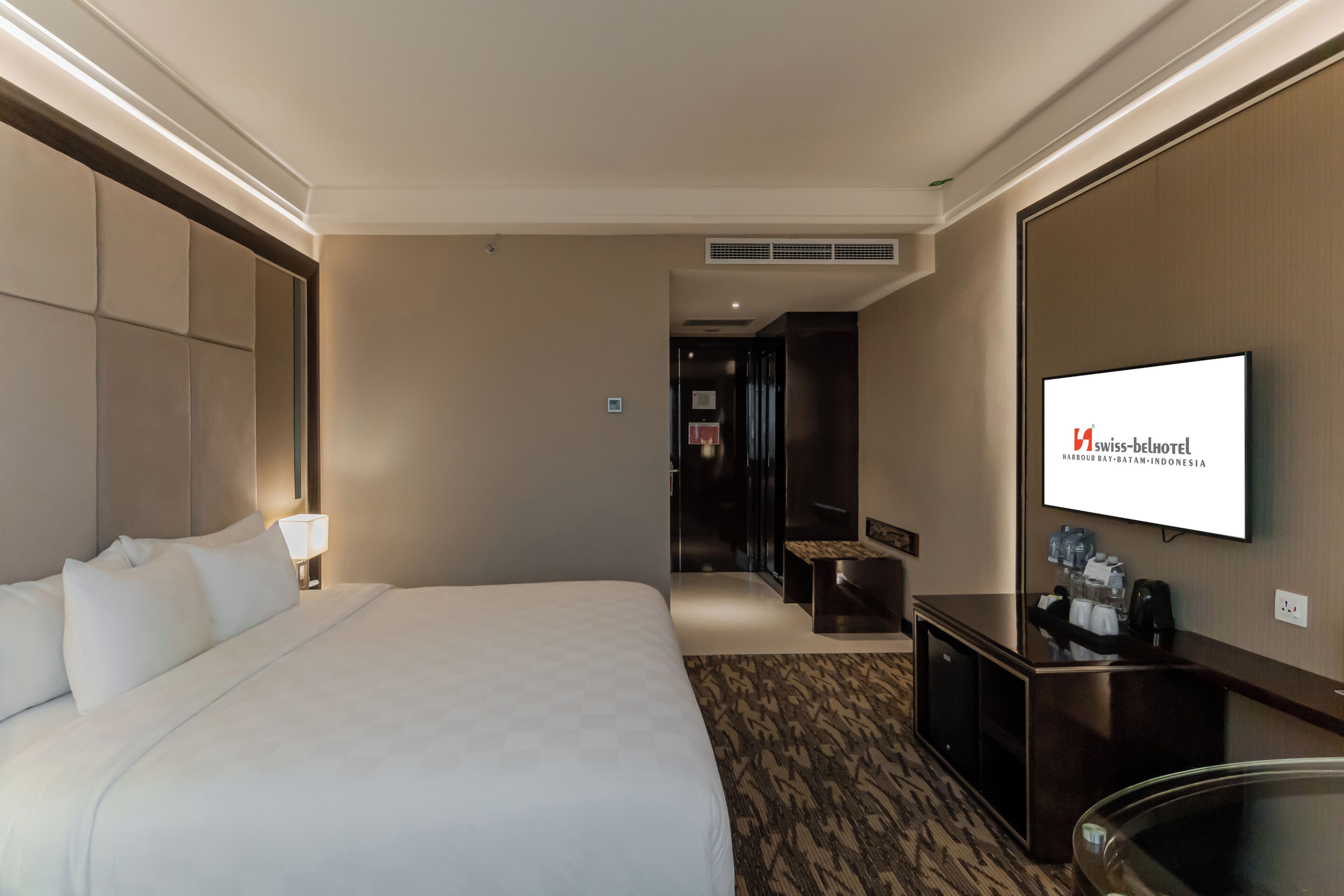 A hotel room with a large bed, a desk, a television, and a minibar.