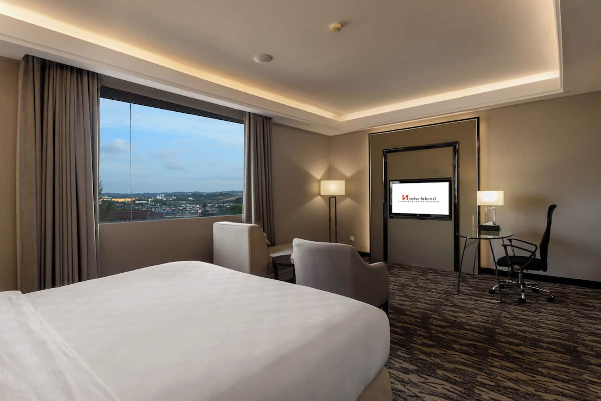 Een hotelkamer met een groot bed, twee stoelen, een bureau en een televisiescherm waarop de naam van het hotel staat.