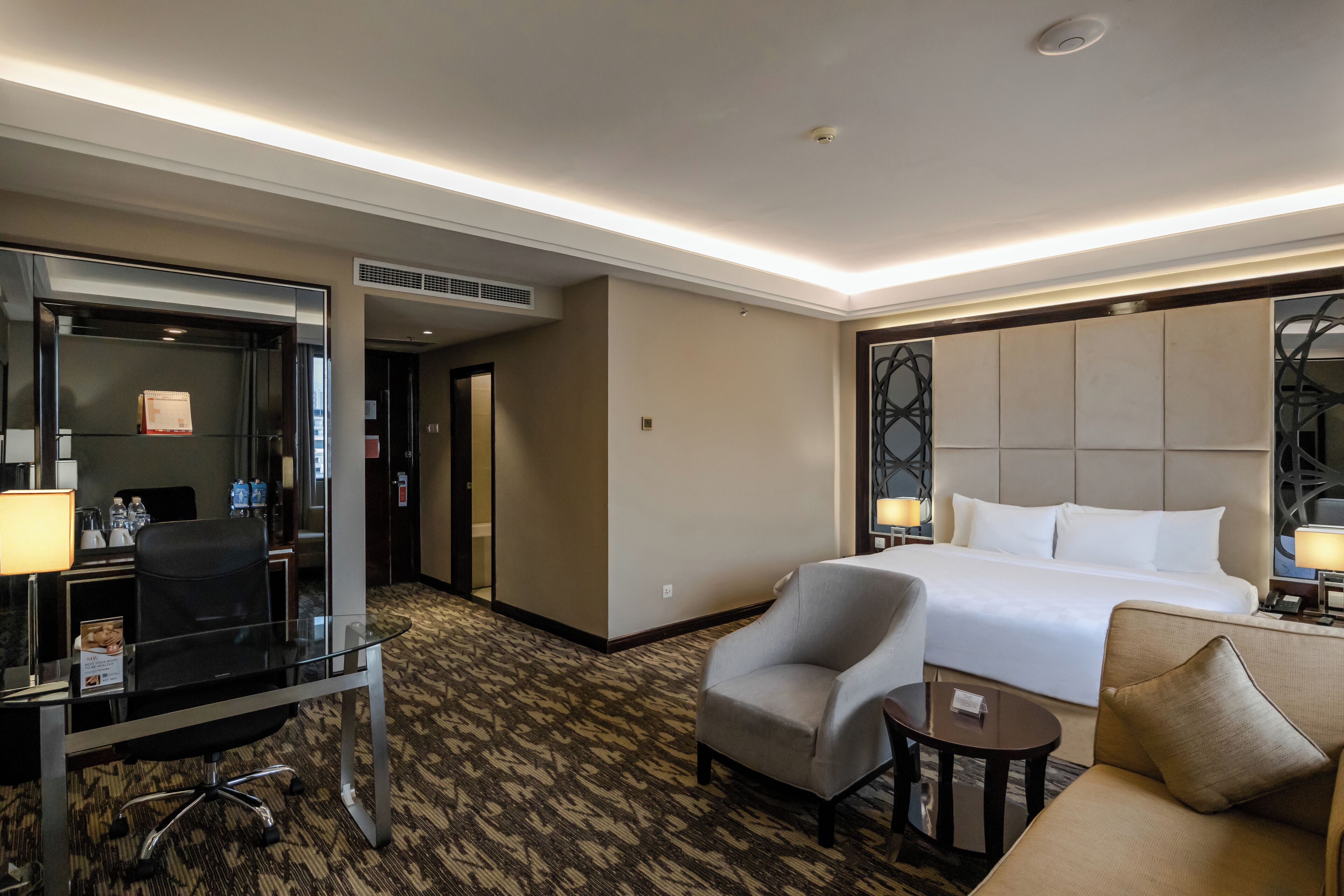 Quarto de hotel com cama, escrivaninha com cadeira, mesinha e sofá.