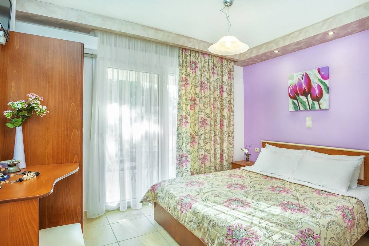 Una camera da letto con un letto, una scrivania, una sedia, un vaso con fiori e un quadro appeso al muro.
