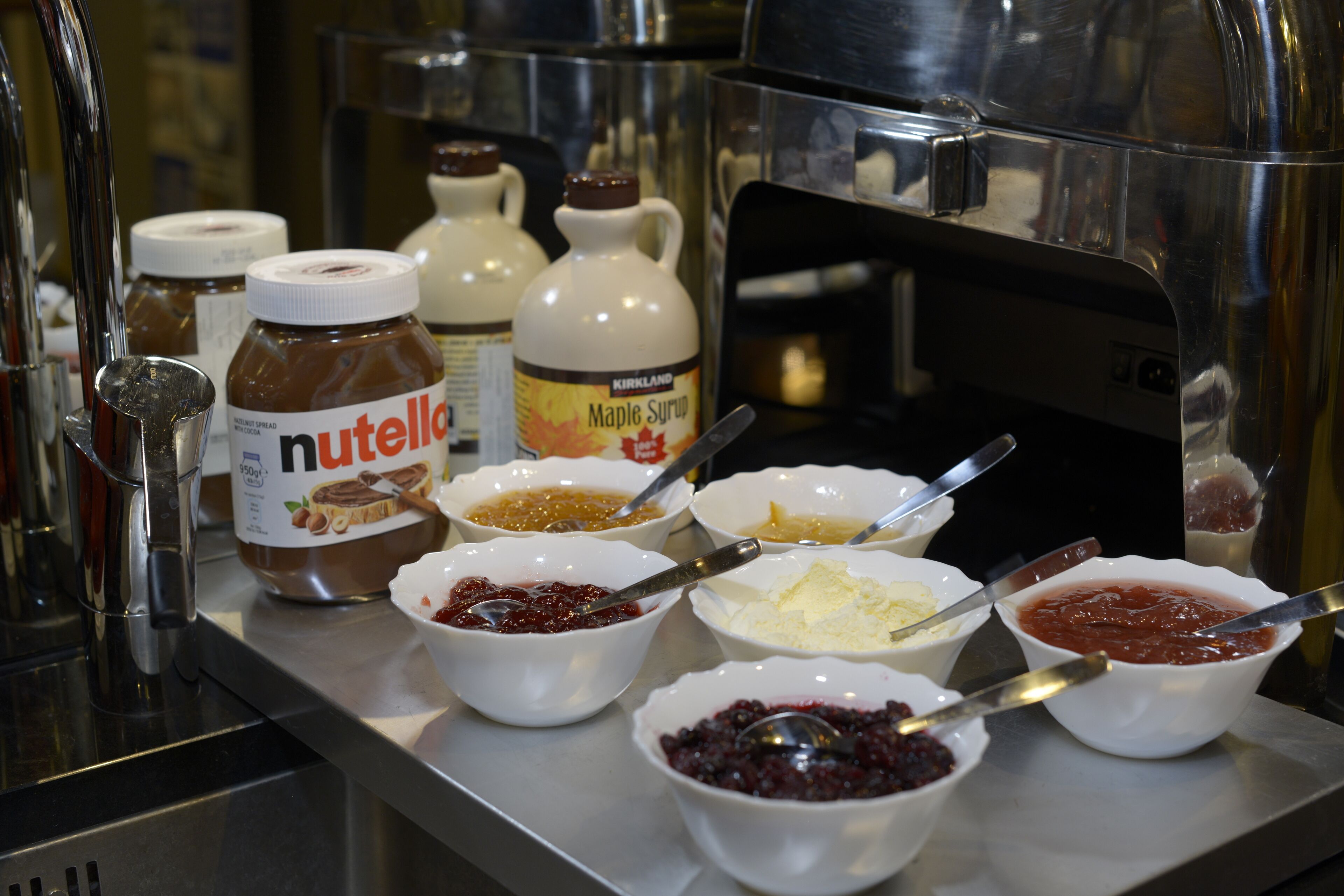 A buffet table with various food items and condiments, including jars of Nutella and Maple Syrup.