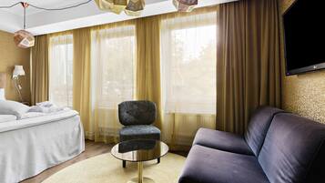 A modern hotel room with a bed, a round coffee table, a sofa, and a TV mounted on the wall.