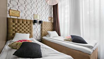 A hotel room with two beds, a tufted headboard, a patterned wall, and a large window with curtains.